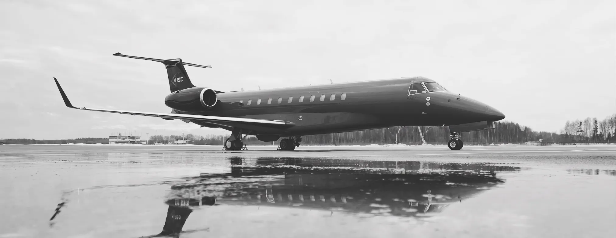 A business jet parked on a wet apron, mirrored in standing water