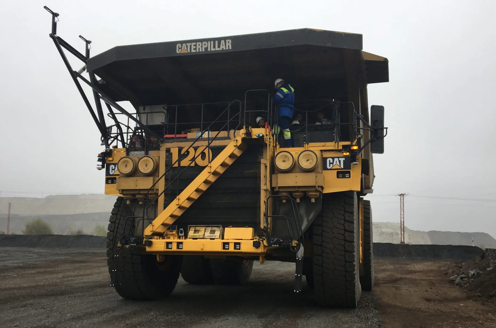 A Caterpillar haul truck fitted with autonomy sensor masts on a foggy mine haul road, engineers on the access deck