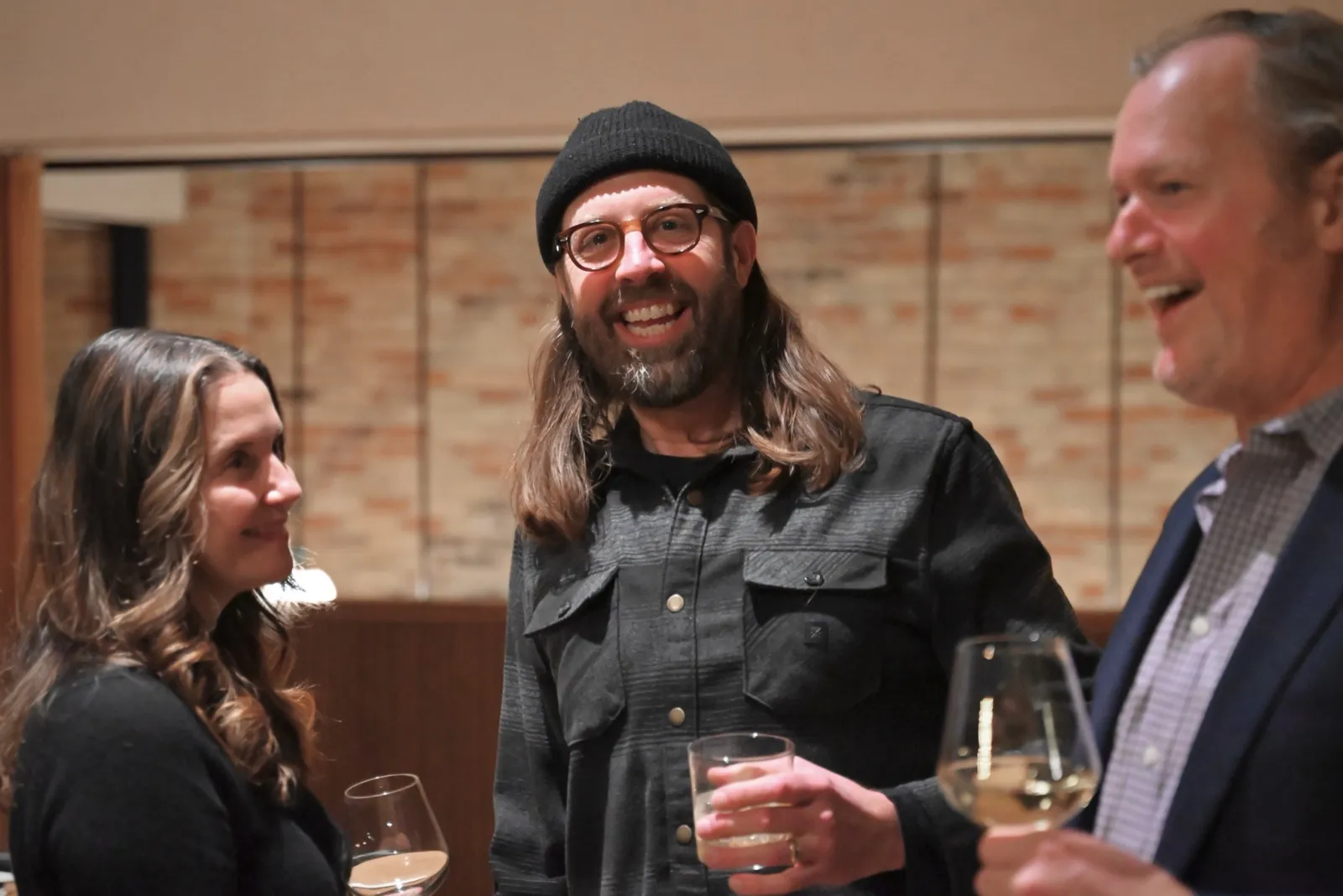 Three colleagues laughing over drinks at an evening get-together