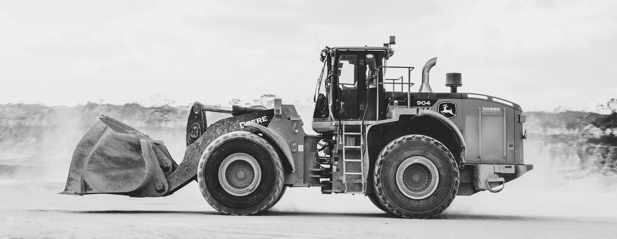 A wheel loader crossing a dusty yard at speed