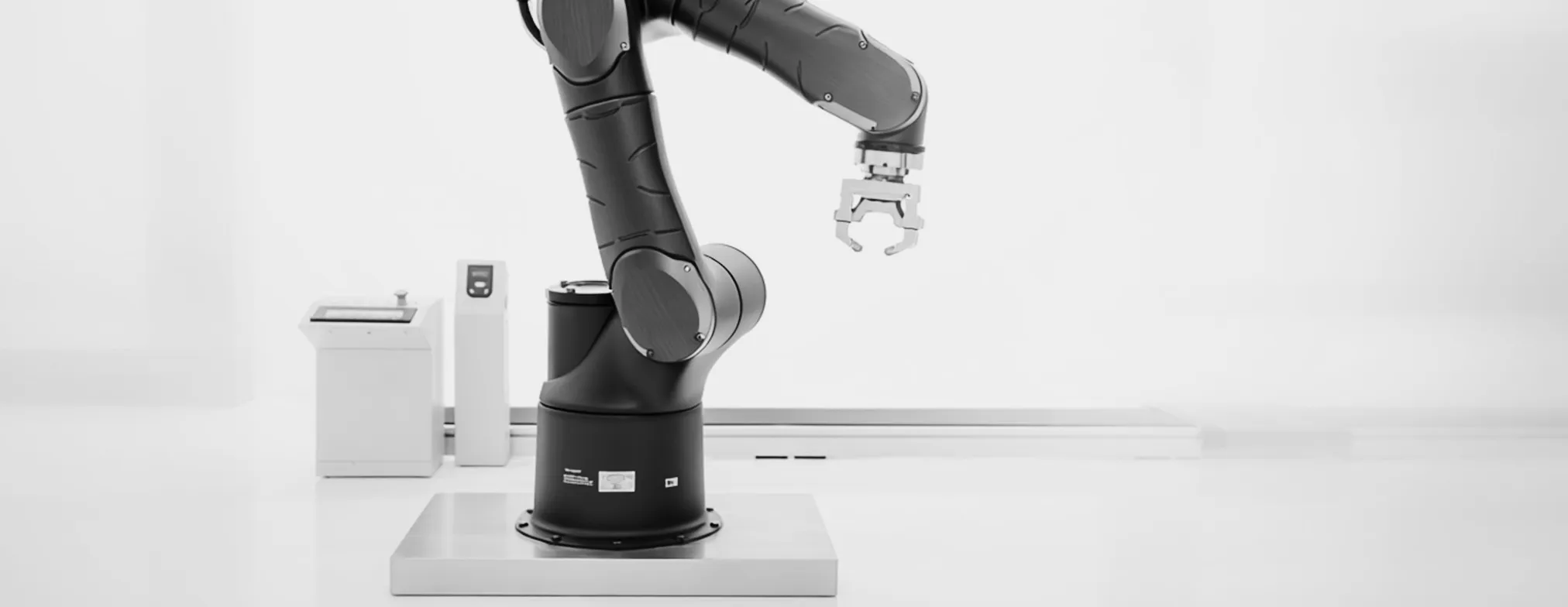 A robotic arm with a gripper poised over a steel work plate in a bright lab