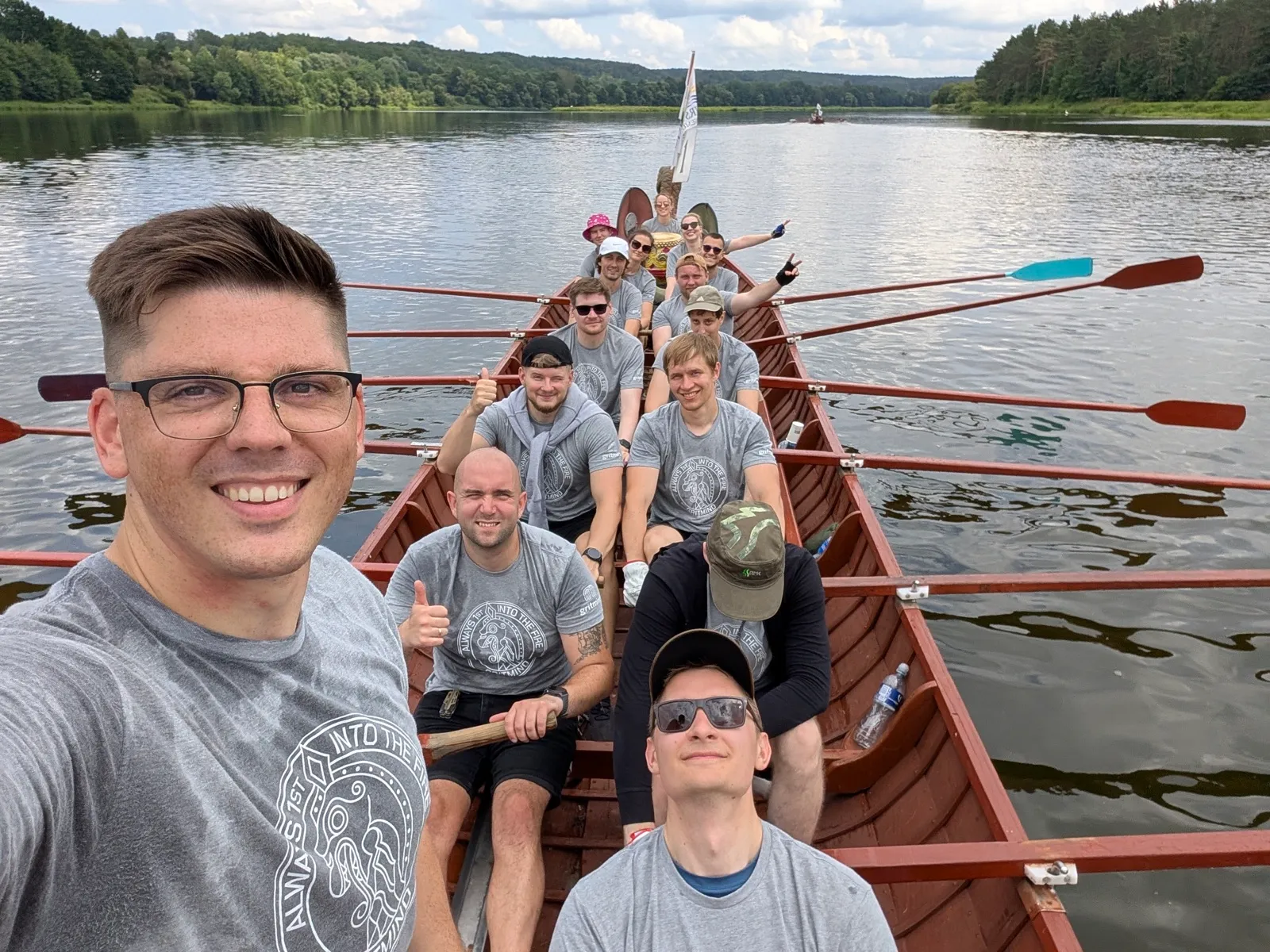 The team rowing a wooden longboat down a river, oars out on both sides