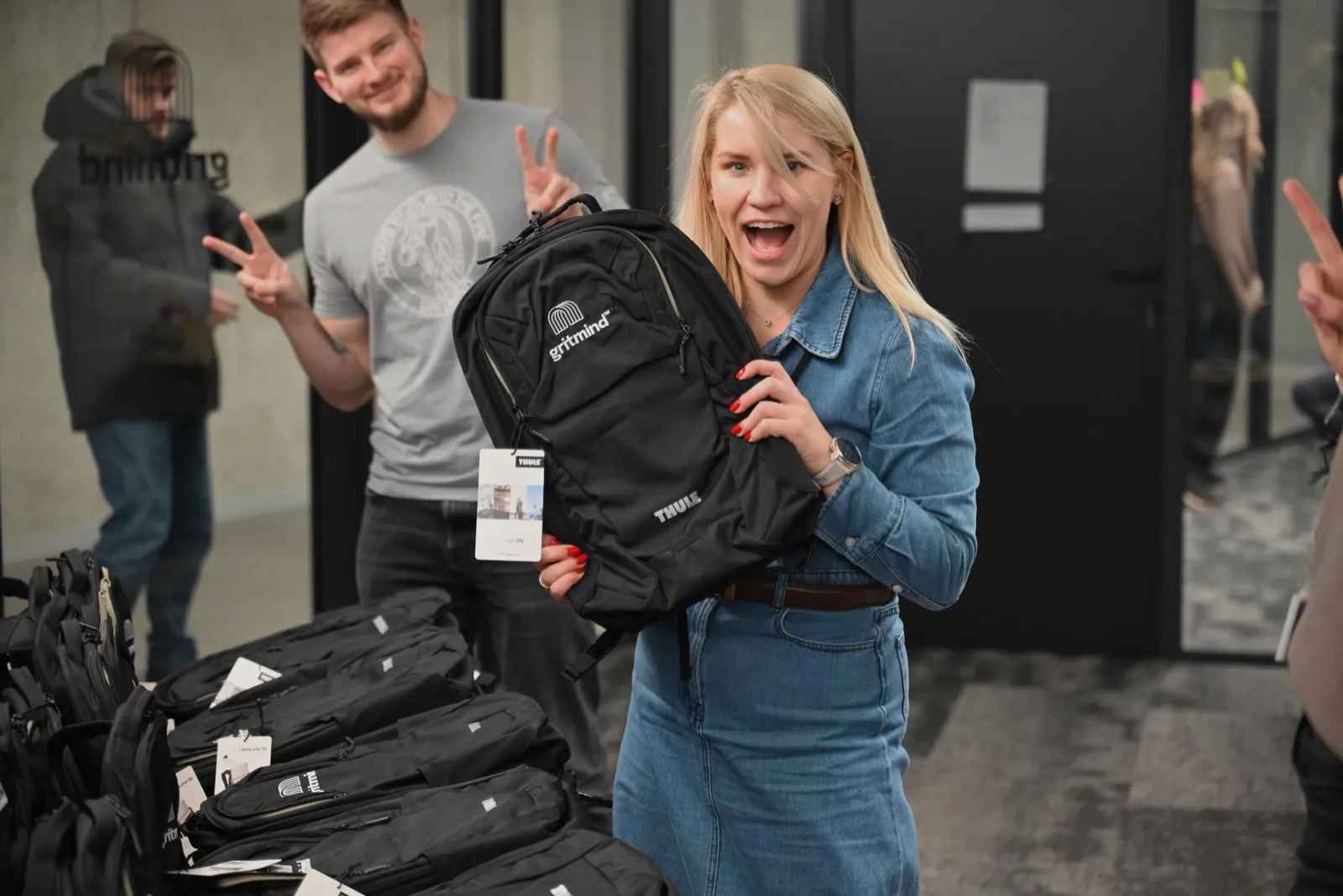 A colleague celebrating a new gritmind backpack while another flashes peace signs