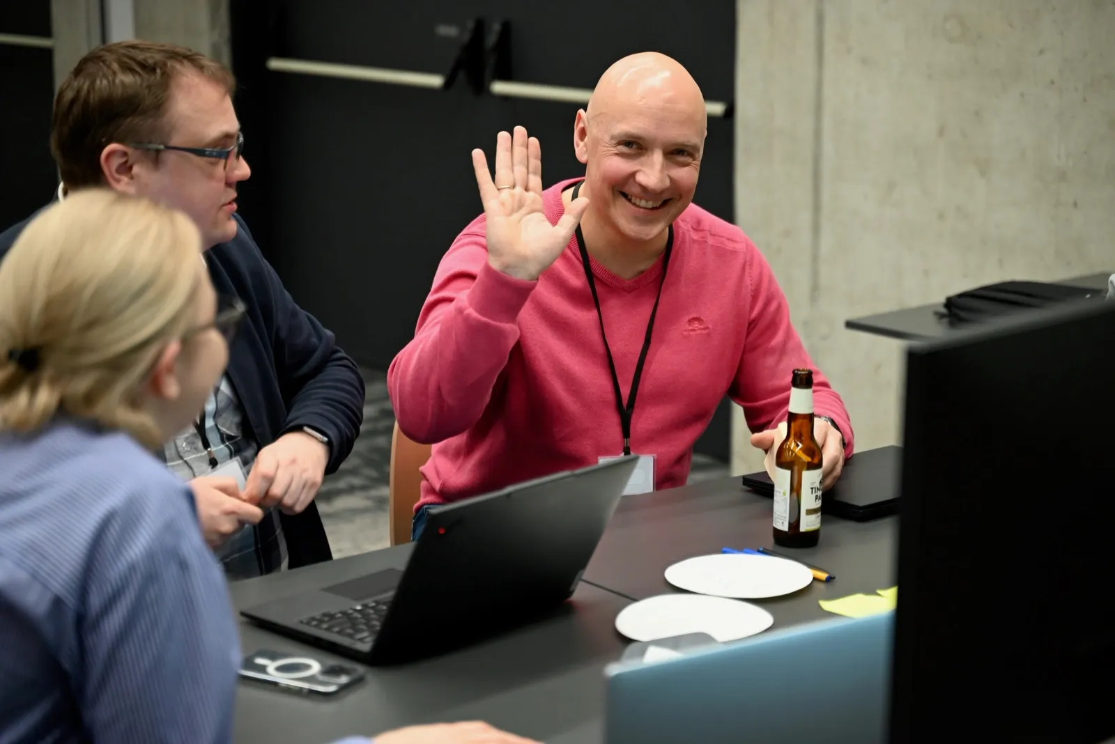 A smiling engineer waving mid-discussion at a workshop table
